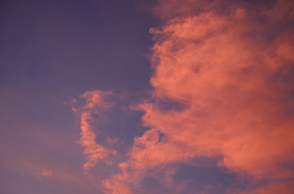Glowing orange/pink sunset on an evening blue sky. Tiny plane.